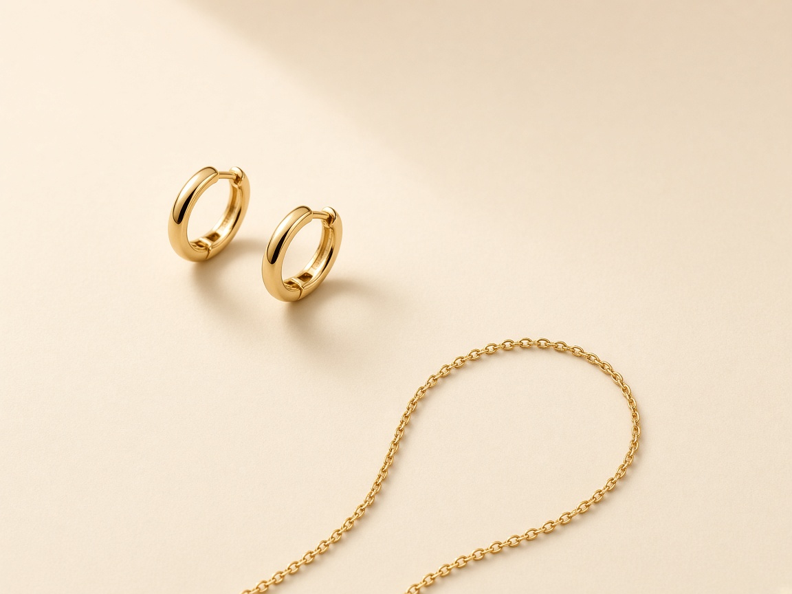 Gold hoop earrings and a thin gold chain on a seamless cream background